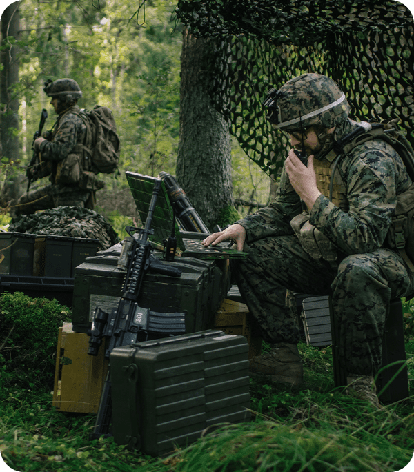 Soldiers communicating in forested military setting.